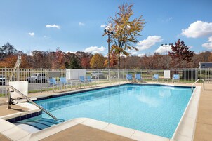 Piscina rectangular con borde de azulejos, rodeada por una valla blanca y una zona de terraza con sillas.
