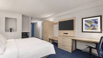 A hotel room with a bed, a desk, a chair, a TV, a microwave, and a framed picture on the wall.