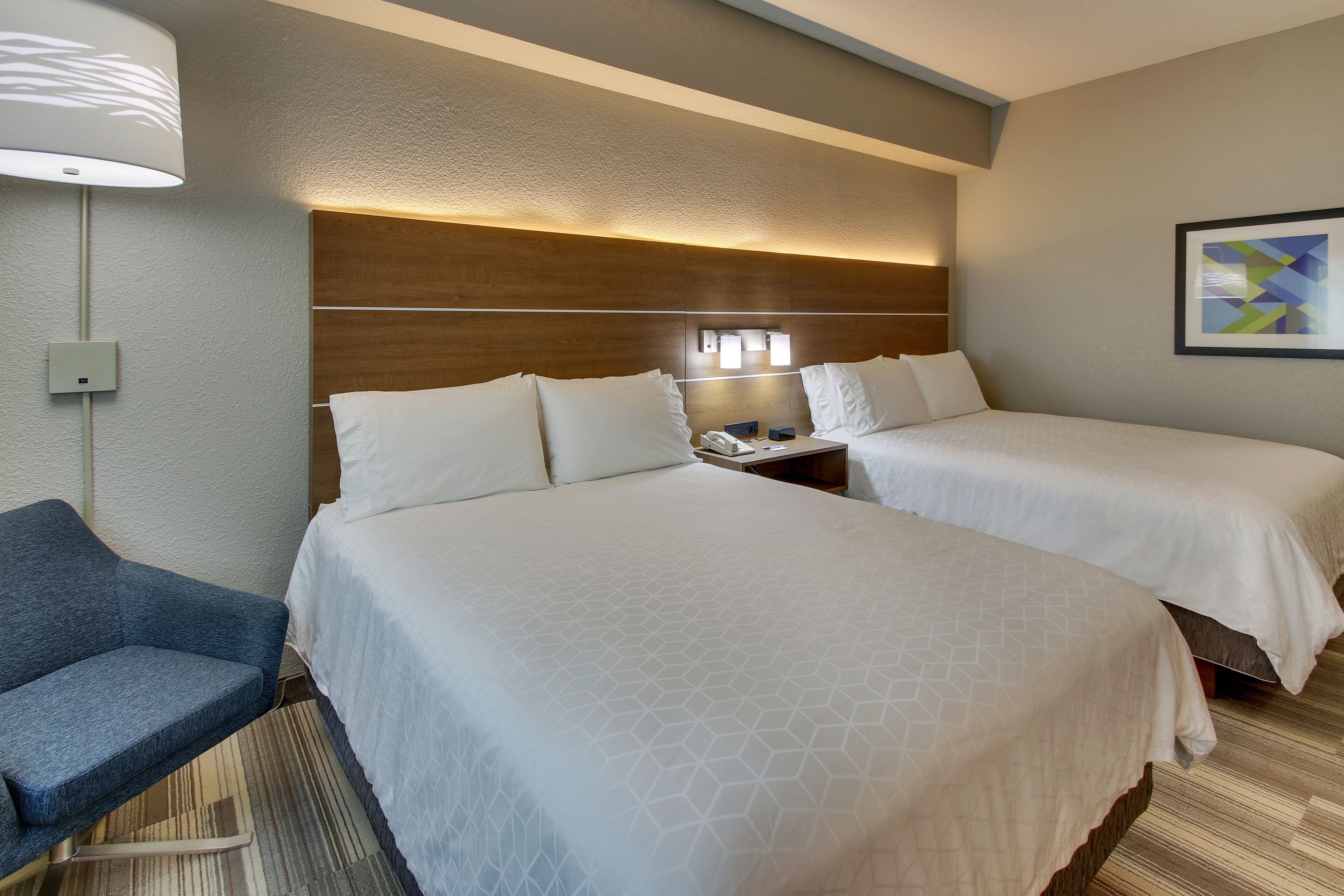 Une chambre d’hôtel avec deux lits, un bureau, une chaise, une lampe et un tableau au mur.