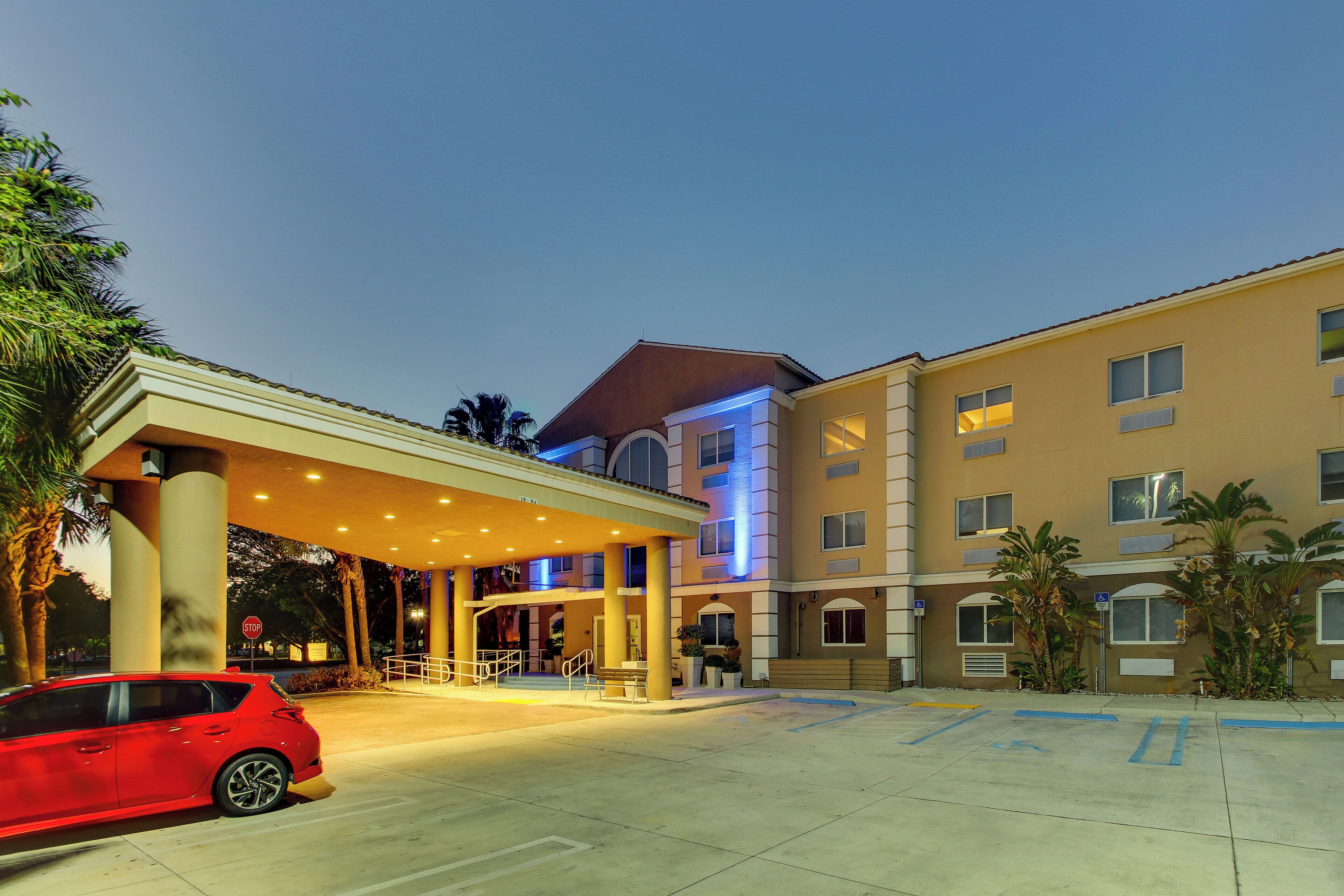 A hotel entrance with a covered area, a red car parked, and a clear sky.