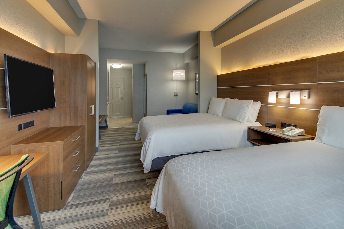 Habitación de hotel con dos camas, un escritorio, un televisor y un baño a la vista.