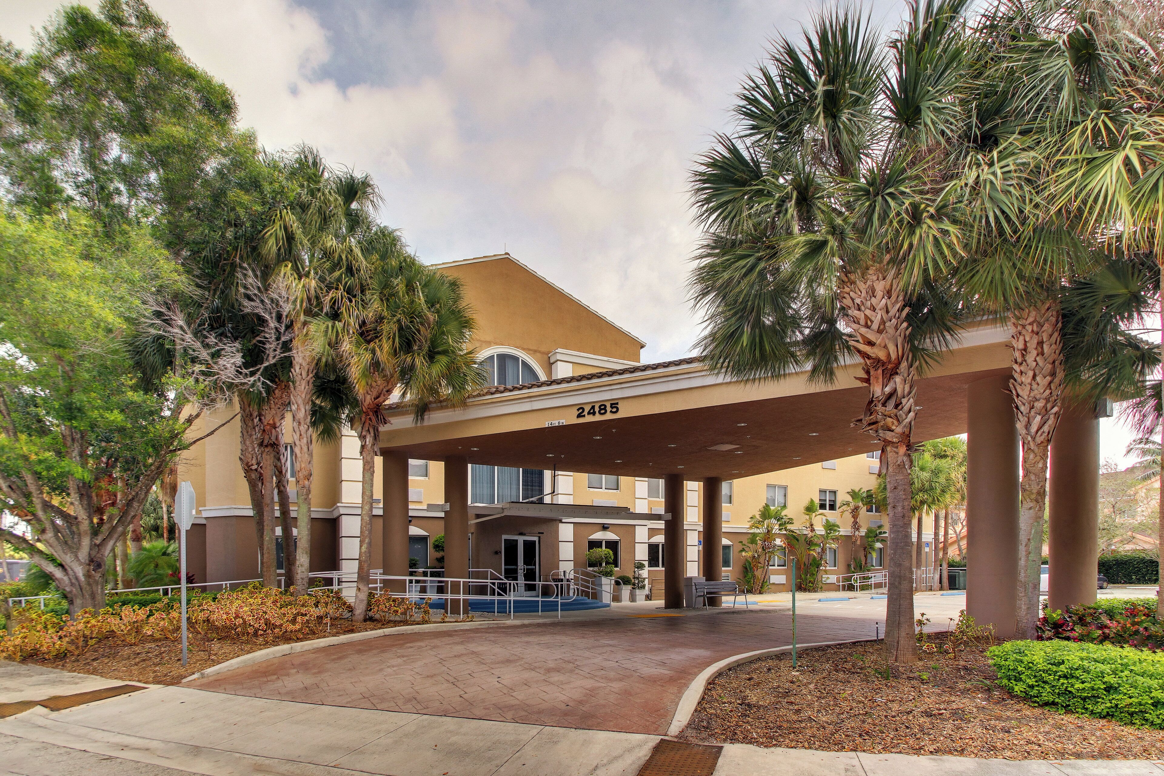 A hotel entrance with a covered walkway, palm trees, and a clear sky.