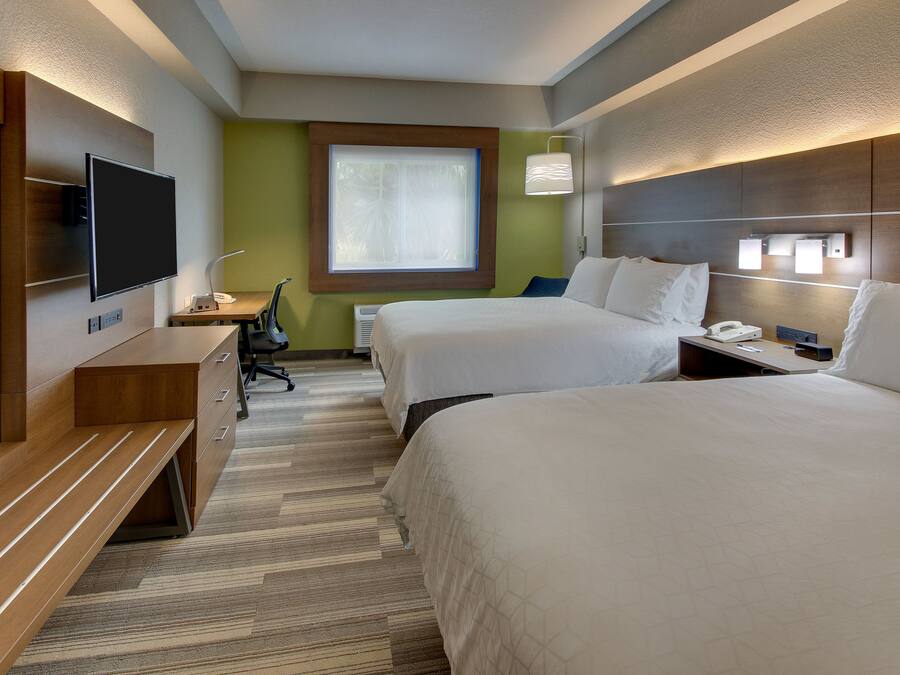 Een hotelkamer met twee bedden, een bureau met een stoel, een flatscreen televisie, een raam en een wandlamp.