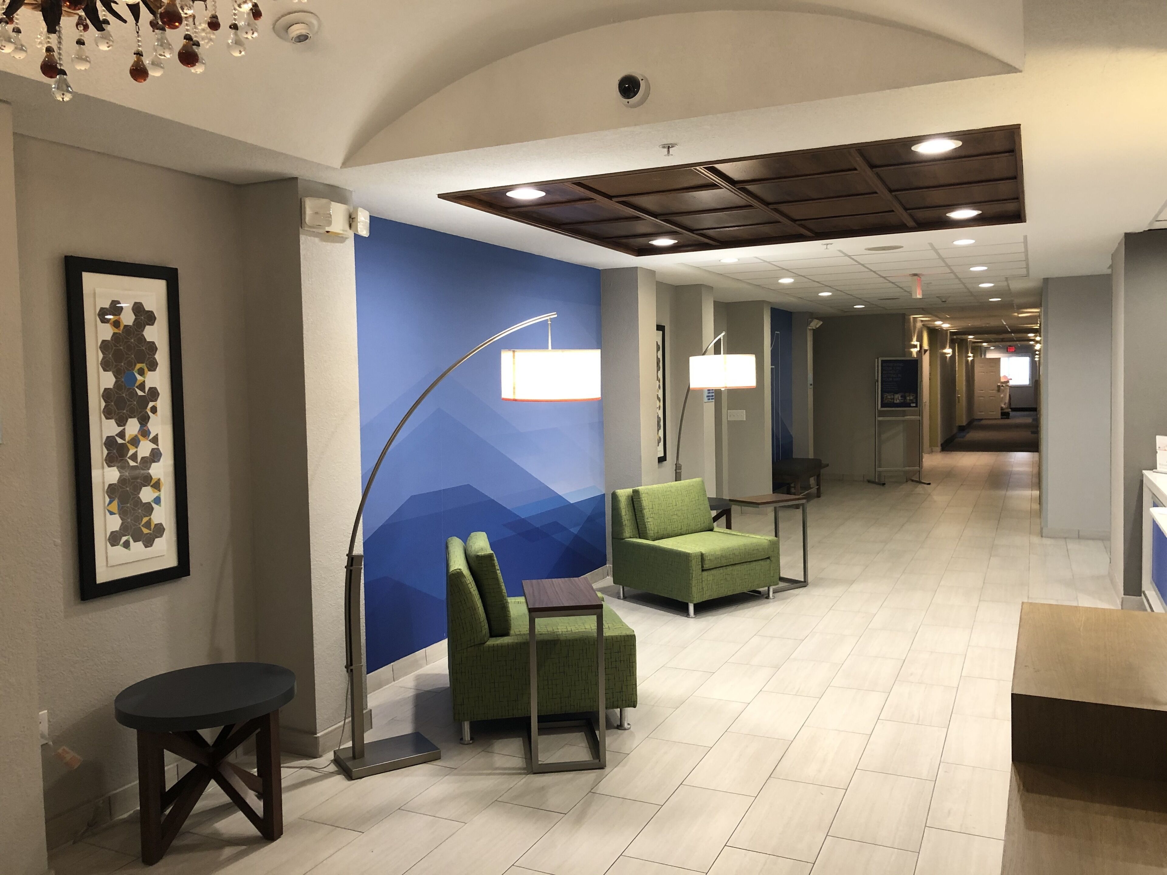A hotel lobby with a blue wall, green seating, a framed artwork, and a modern ceiling design.