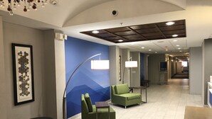 Hotellin aula, jossa on sininen seinä, vihreät istuimet, kehystetty taideteos ja moderni kattorakenne.