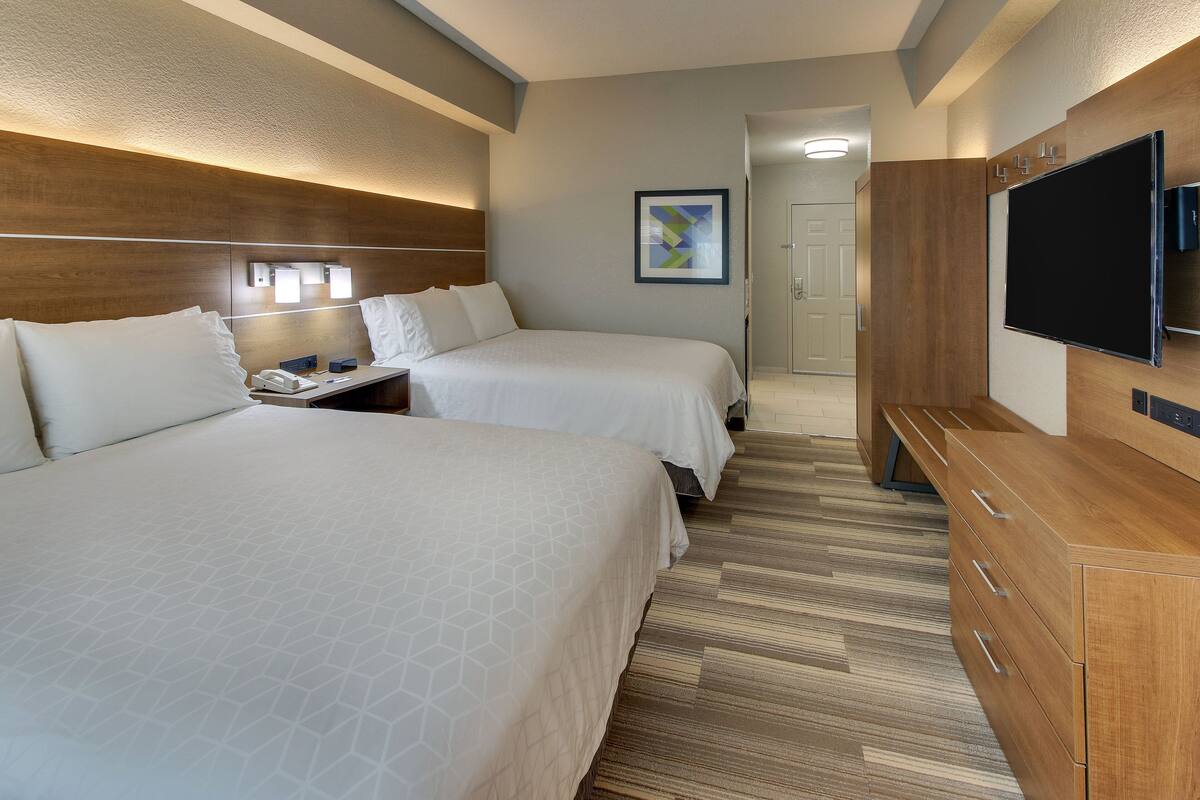 Habitación de hotel con dos camas, un escritorio con teléfono, televisión y cómoda de madera.