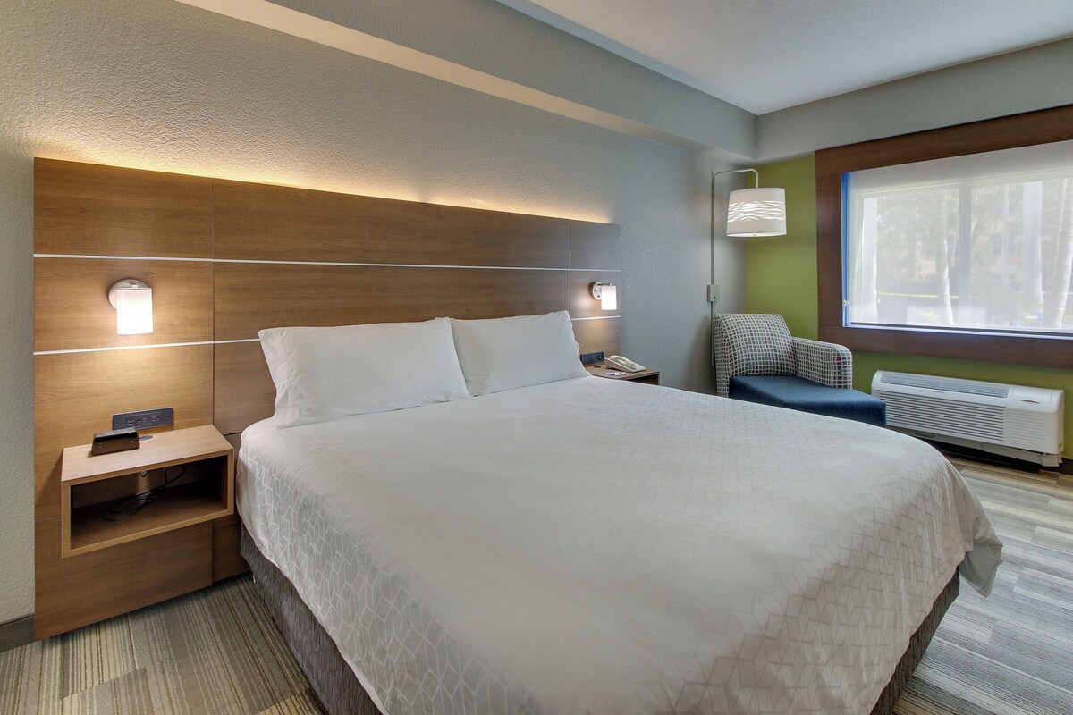 Een hotelkamer met een groot bed, nachtkastjes, een stoel, een raam met uitzicht en een airconditioning.