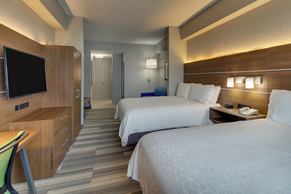 Een hotelkamer met twee bedden, een bureau, een televisie en een badkamer in de verte.
