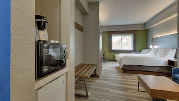 A hotel room with a kitchenette, a bed, a desk, and a window with a view.