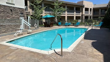 Una piscina rectangular con una escalera metálica, rodeada de sillas de descanso y un patio con baldosas de piedra.