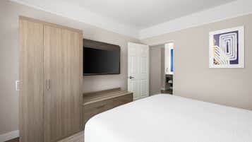 Habitación de hotel con una cama grande, un armario, un televisor fijado a la pared y una puerta que da a otra habitación.