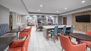 A modern dining area with a long table and orange chairs, a smaller table with blue chairs, and a TV mounted on the wall. - Holiday Inn Express Hotel & Suites San Dimas by IHG (San Dimas)