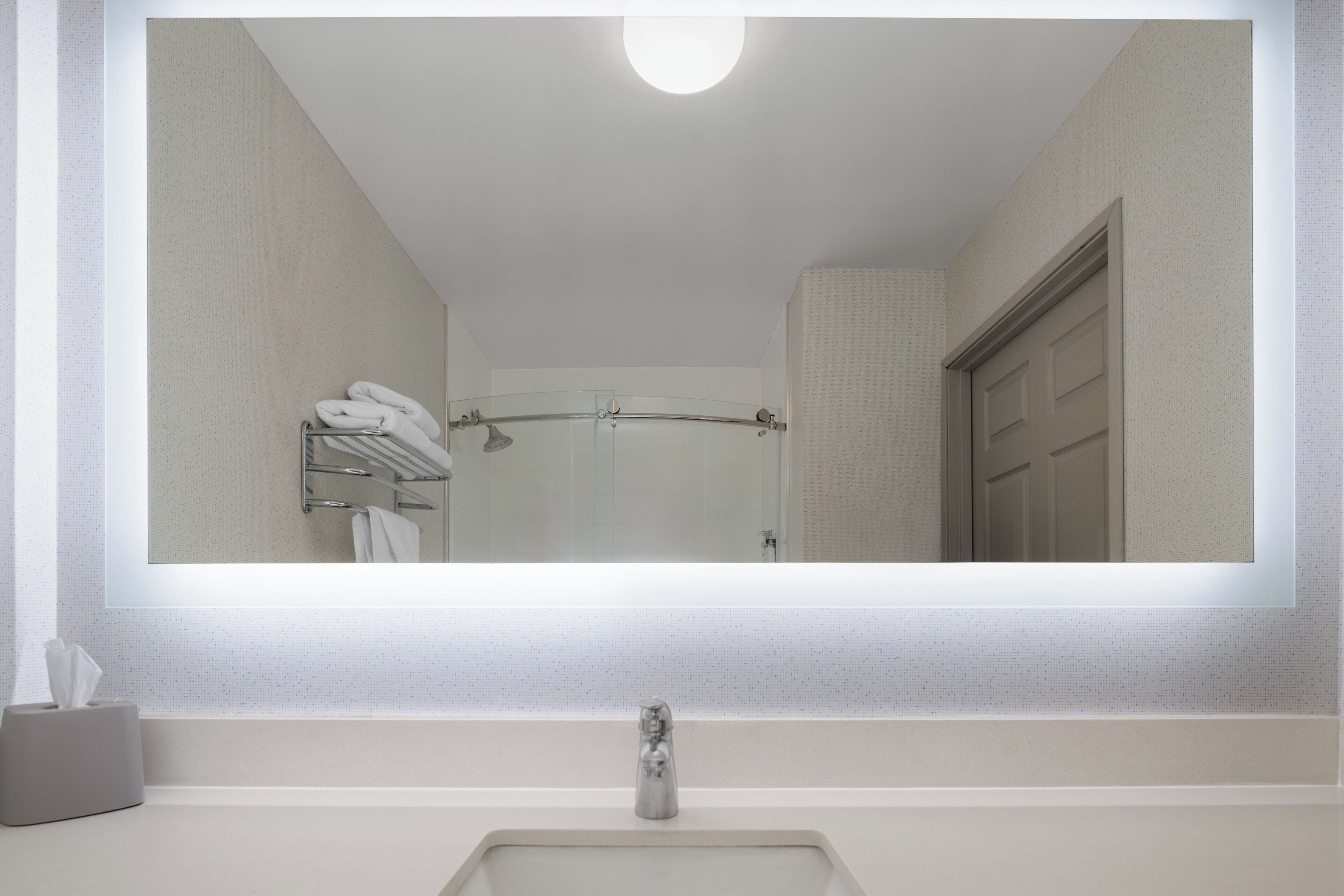 A bathroom with a large mirror, a towel rack, a shower, and a door.