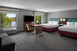 Habitación de hotel con escritorio, dos camas, televisor y vistas al lago.