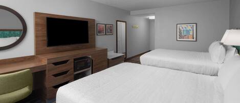 A hotel room with a TV, two beds, a desk with a chair, and a mirror.