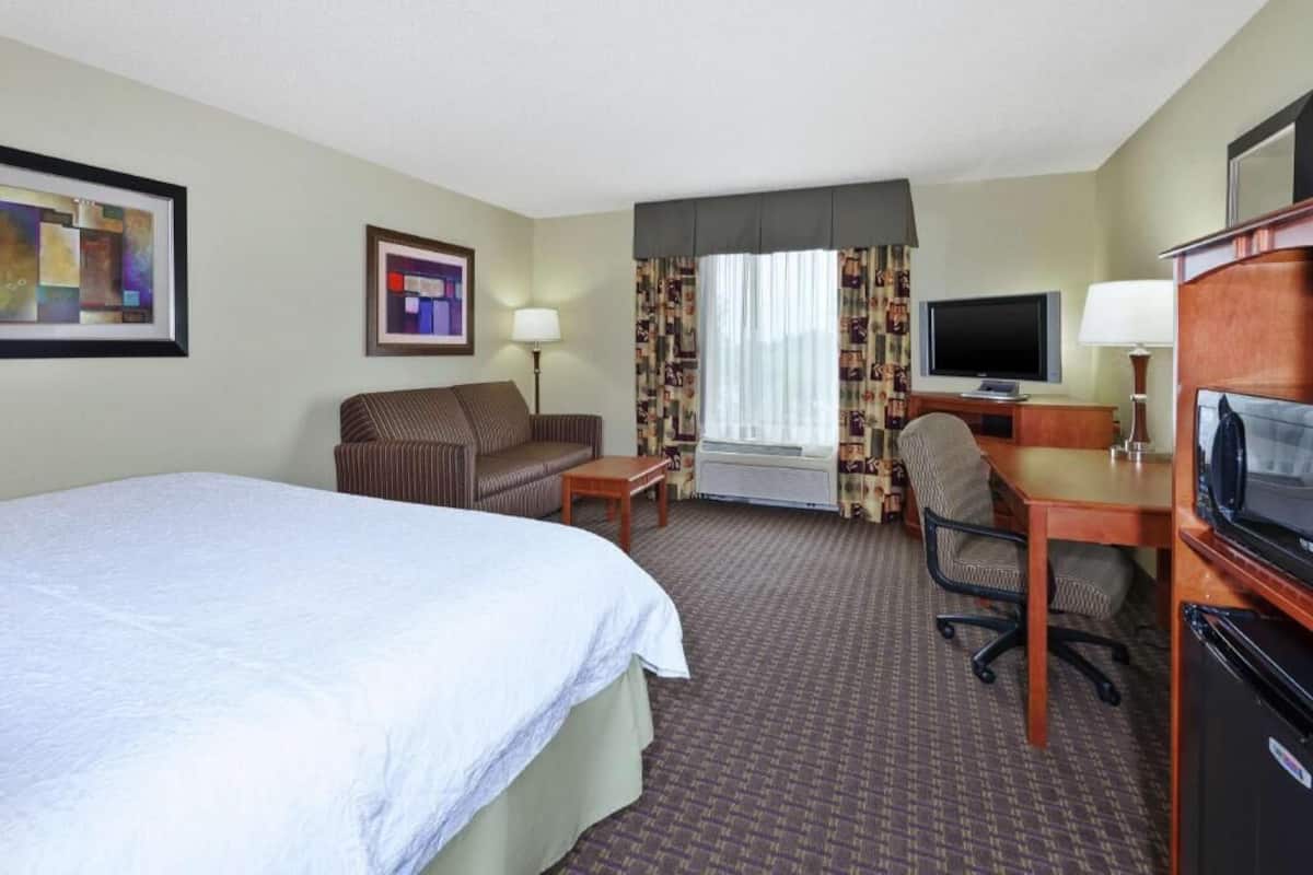 Ein Hotelzimmer mit einem Bett, einem Schreibtisch mit Stuhl, einem Fernseher und einem kleinen Tisch.