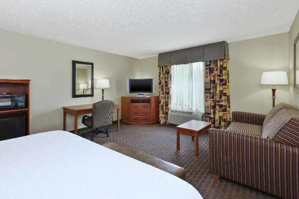 Ein Hotelzimmer mit Bett, Schreibtisch mit Stuhl, Fernseher, Kommode und Sofa.