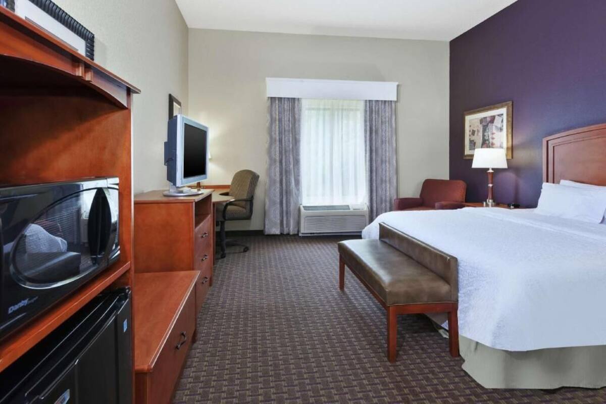 Ein Hotelzimmer mit einem Bett, einem Schreibtisch, einem Fernseher, einem Sessel und einer Klimaanlage.