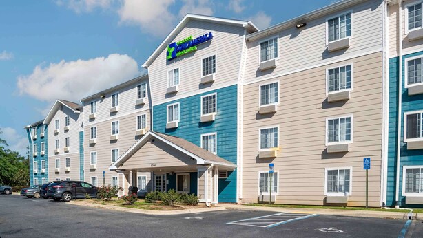 A multi-story hotel with a blue and beige exterior, a covered entrance, and a parking lot with marked handicapped spaces. - Extended Stay America Select Suites - Tallahassee - Northwest (Tallahassee)