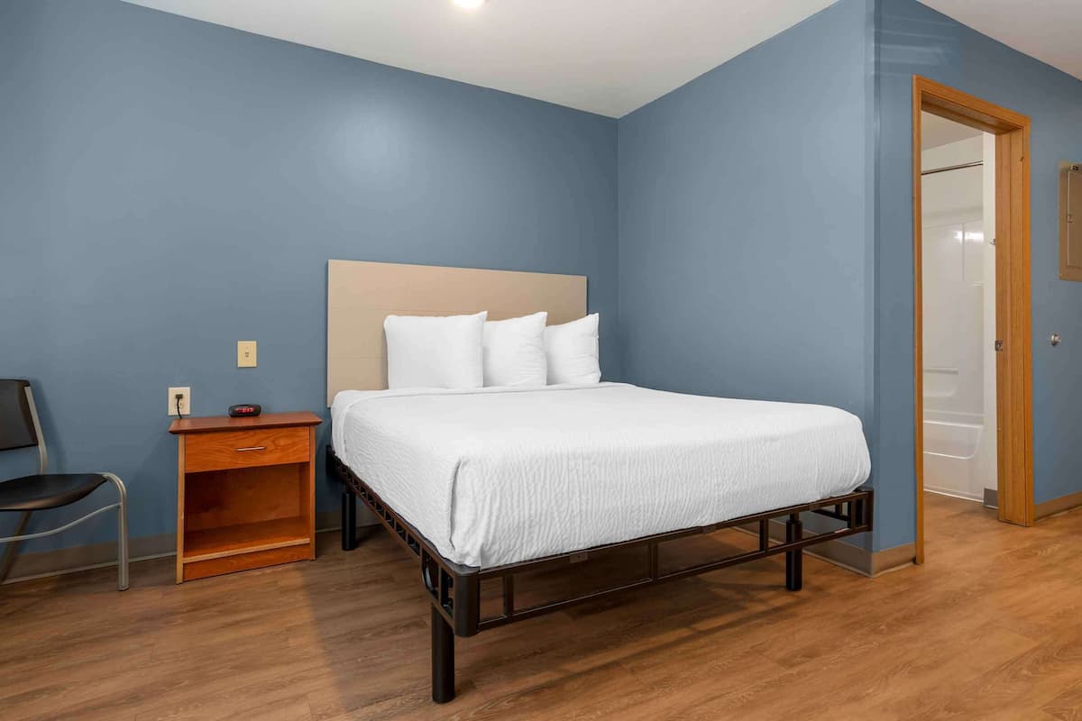 A bedroom with a bed, a nightstand, a chair, and a wooden floor.
