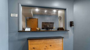 A hotel reception area with a wooden desk, a mirror above it, and a sign indicating doors are locked 24 hours. - Extended Stay America Select Suites - Tallahassee - Northwest (Tallahassee)