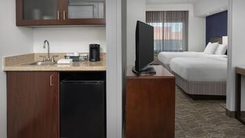 A hotel room with a kitchenette, a TV, two beds, and a view of the city.