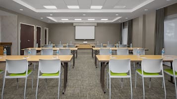 A conference room with a large screen, multiple tables, and chairs.