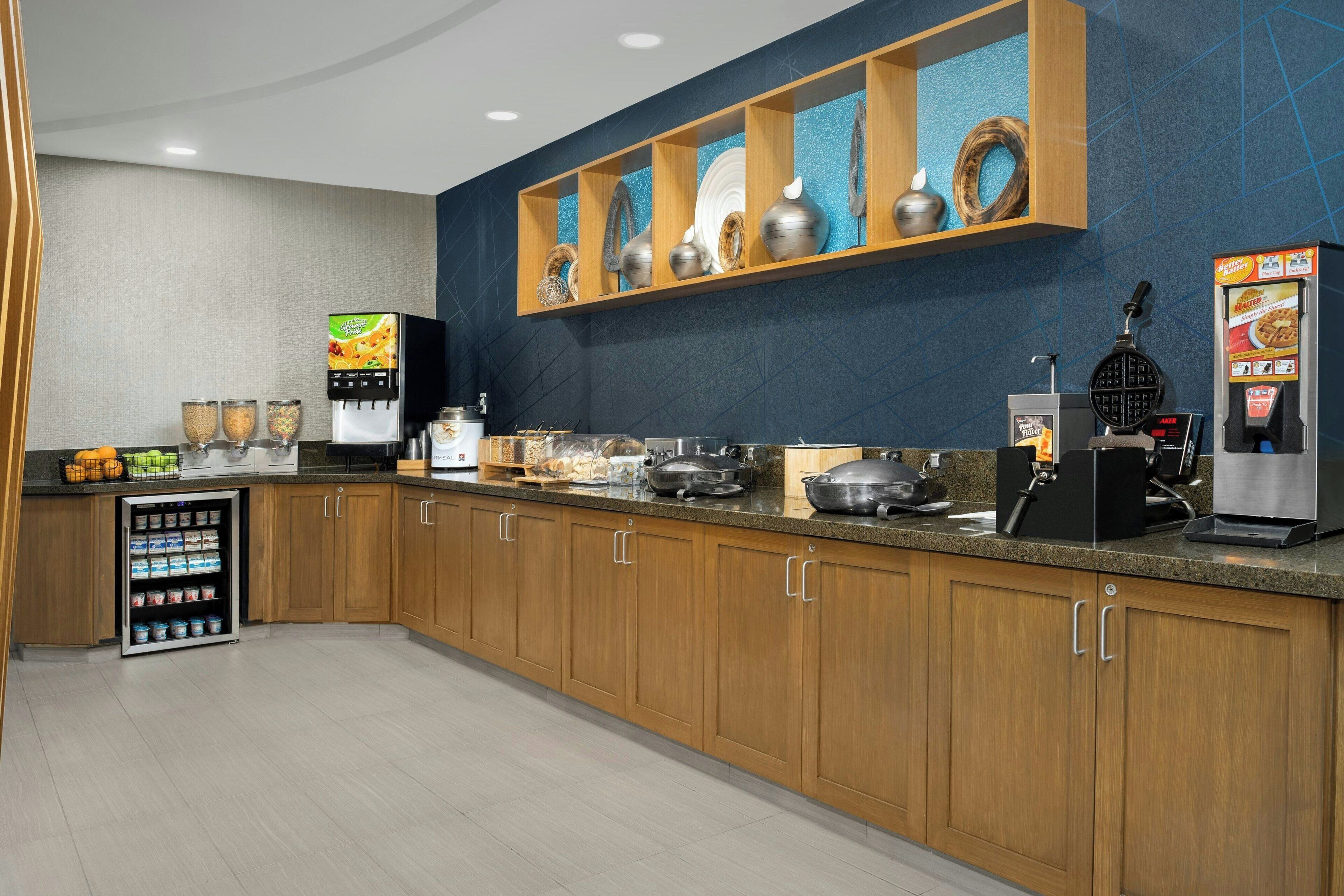 A modern kitchen with wooden cabinets, a built-in coffee machine, and a self-serve beverage station.