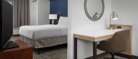 A hotel room with a bed, a desk, a chair, a TV, a lamp, and a mirror.