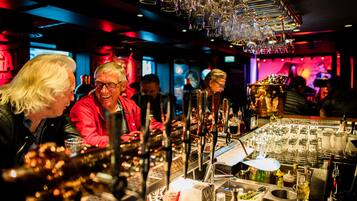 Zona de bar con varios vasos y botellas, una barra y una persona con chaqueta roja.