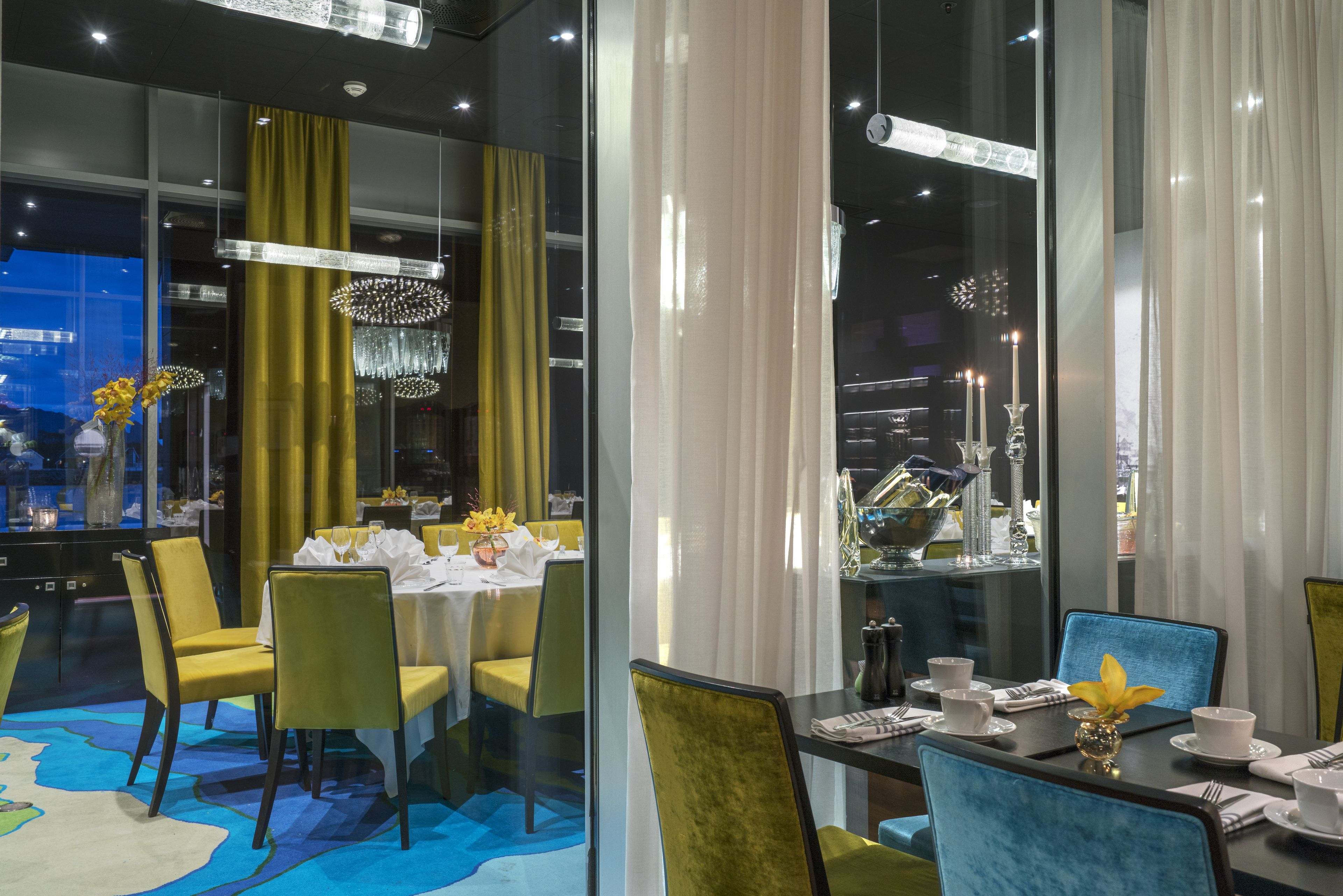 A modern dining area with yellow chairs, a glass table, and a blue chair.