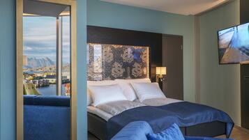 A modern hotel room with a large bed, a view of a scenic landscape, a television, and a seating area with a view of the room.