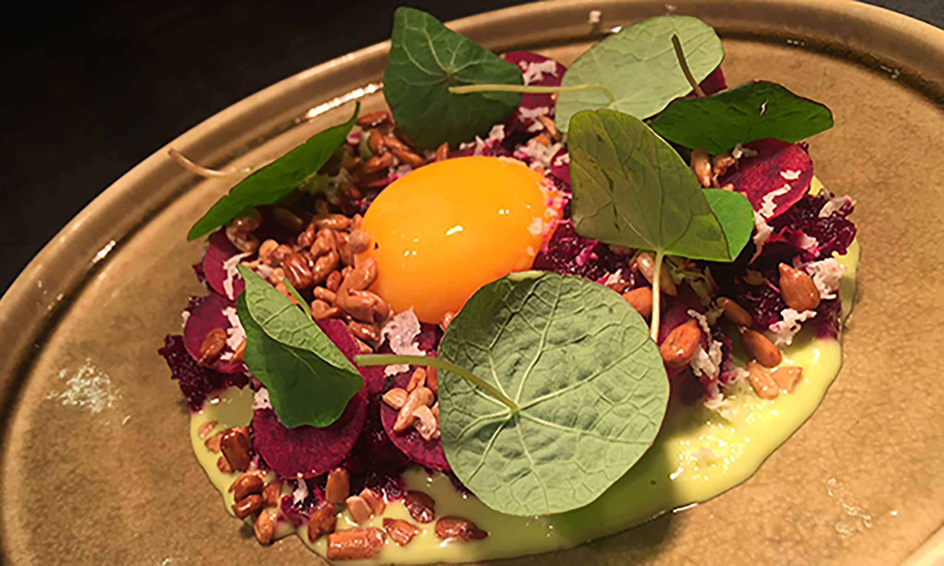 A plated dish with an egg yolk, greens, nuts, and beetroot.