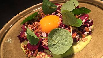 A plated dish with an egg yolk, greens, nuts, and beetroot.