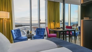 Habitación de hotel con una cama grande, dos sillones, una mesita y vistas a la ciudad.