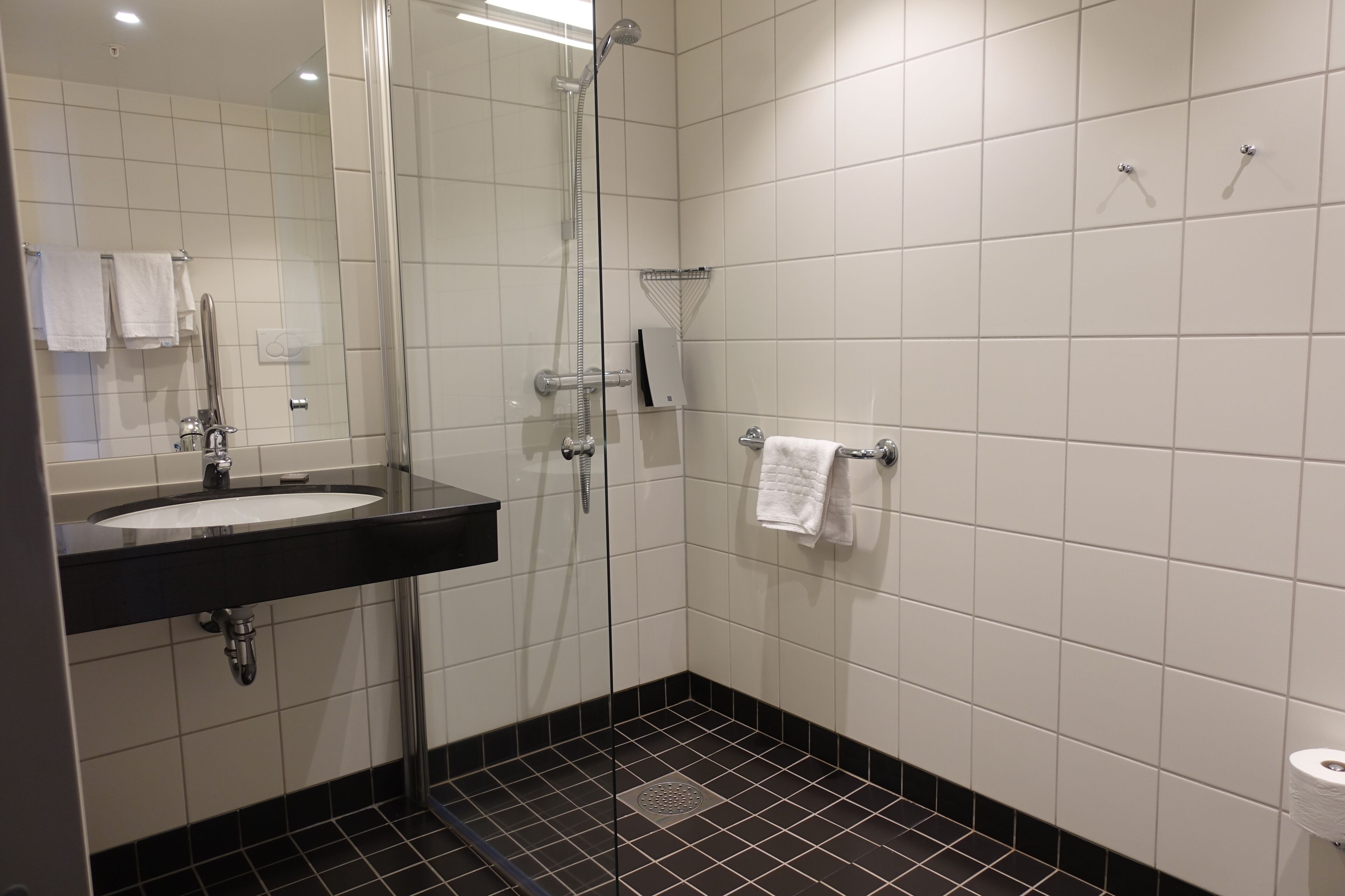 A modern bathroom with a glass-enclosed shower, a sink with a black countertop, and white tiled walls.