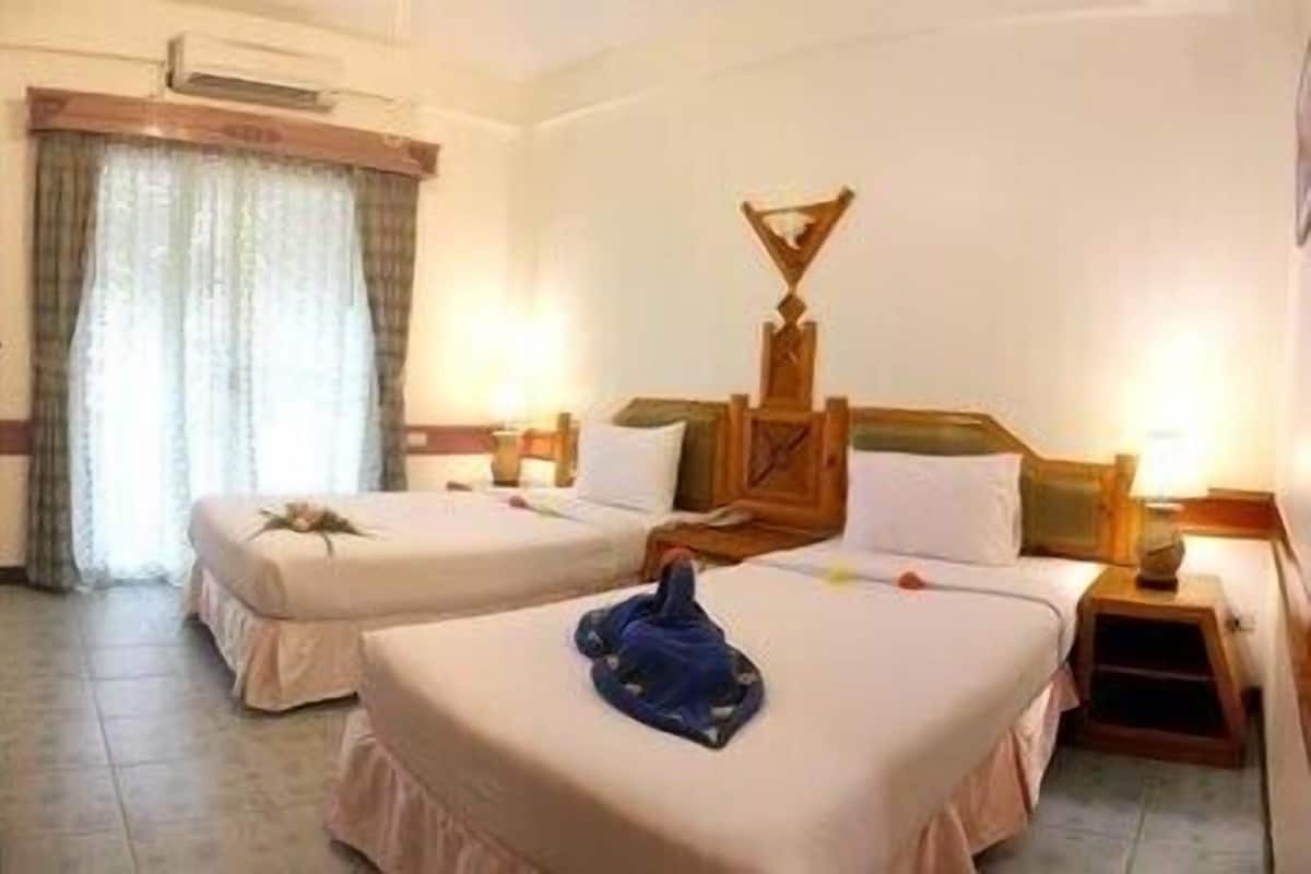 A hotel room with two beds, a wooden headboard, a small table, and a window with curtains.