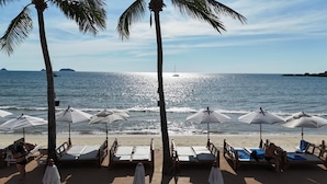 Ein Strand mit Liegestühlen und Sonnenschirmen, Palmen und freiem Blick auf den Ozean.