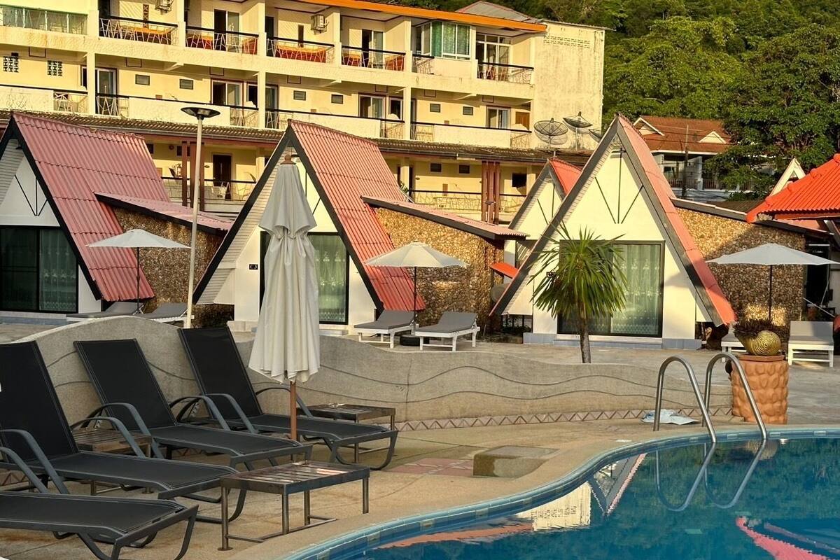 A pool area with lounge chairs and umbrellas, surrounded by buildings with red roofs and balconies.
