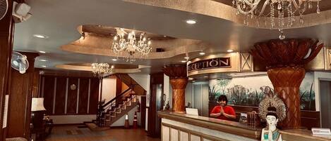 A hotel lobby with a reception desk, a staircase, and a chandelier.