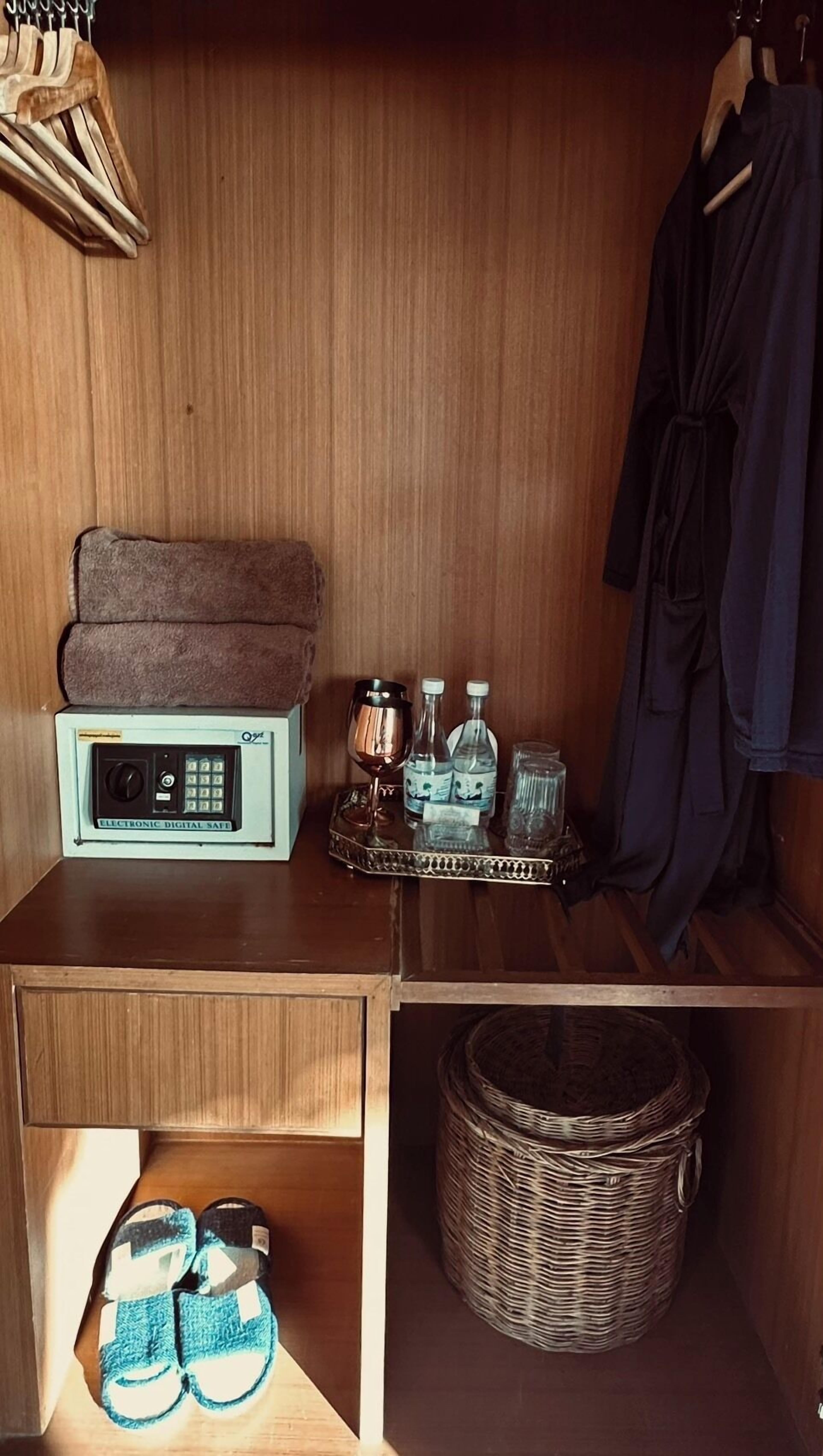 A wooden closet with a digital safe, a wine glass, water bottles, and a wicker basket.