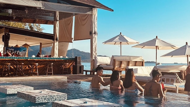 Ein Poolbereich mit Liegestühlen und Sonnenschirmen, eine Bar mit Hockern und Blick auf das Meer.