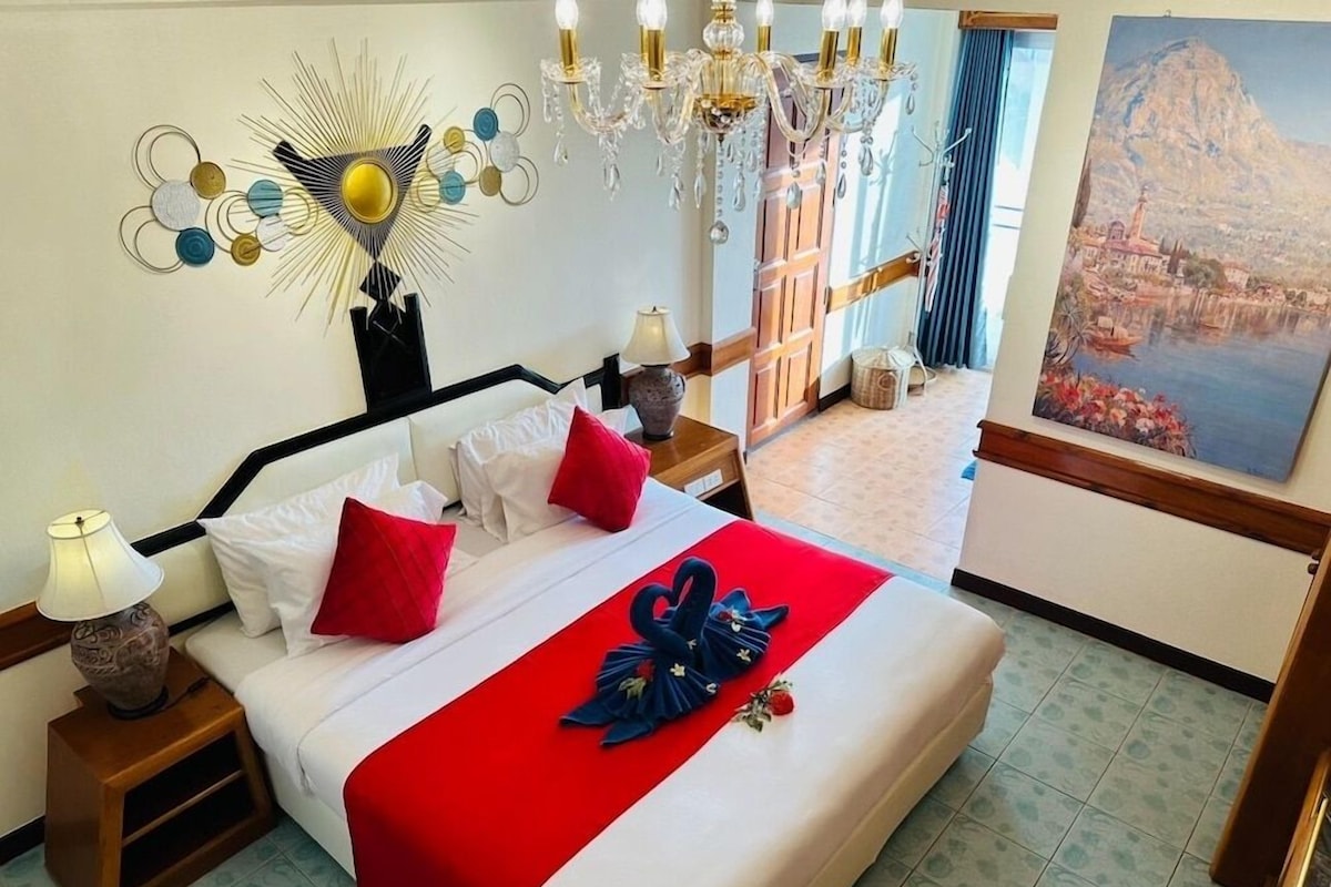 A hotel room with a bed, a chandelier, a painting, and a view of a mountain.