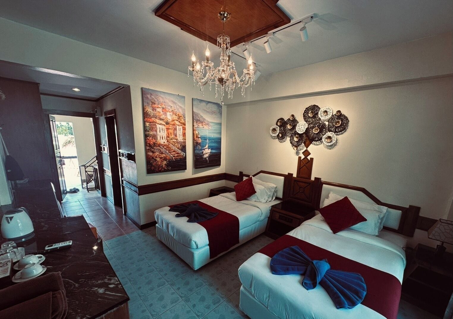A hotel room with two beds, a chandelier, artwork on the wall, and a view of the outside.