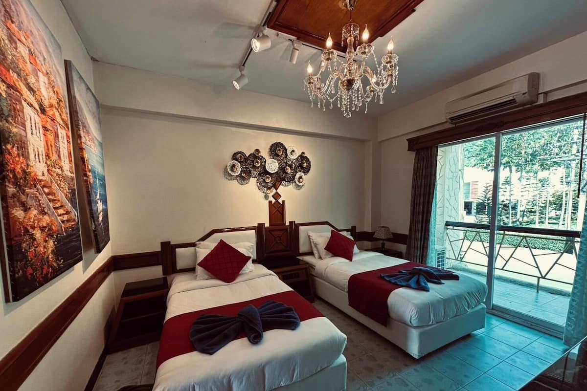 A hotel room with two beds, a chandelier, a large window, and a painting on the wall.