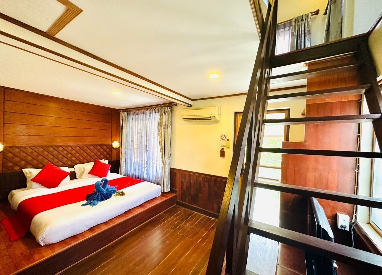 A hotel room with a wooden headboard, a bed with red and white bedding, a wooden floor, and a staircase.