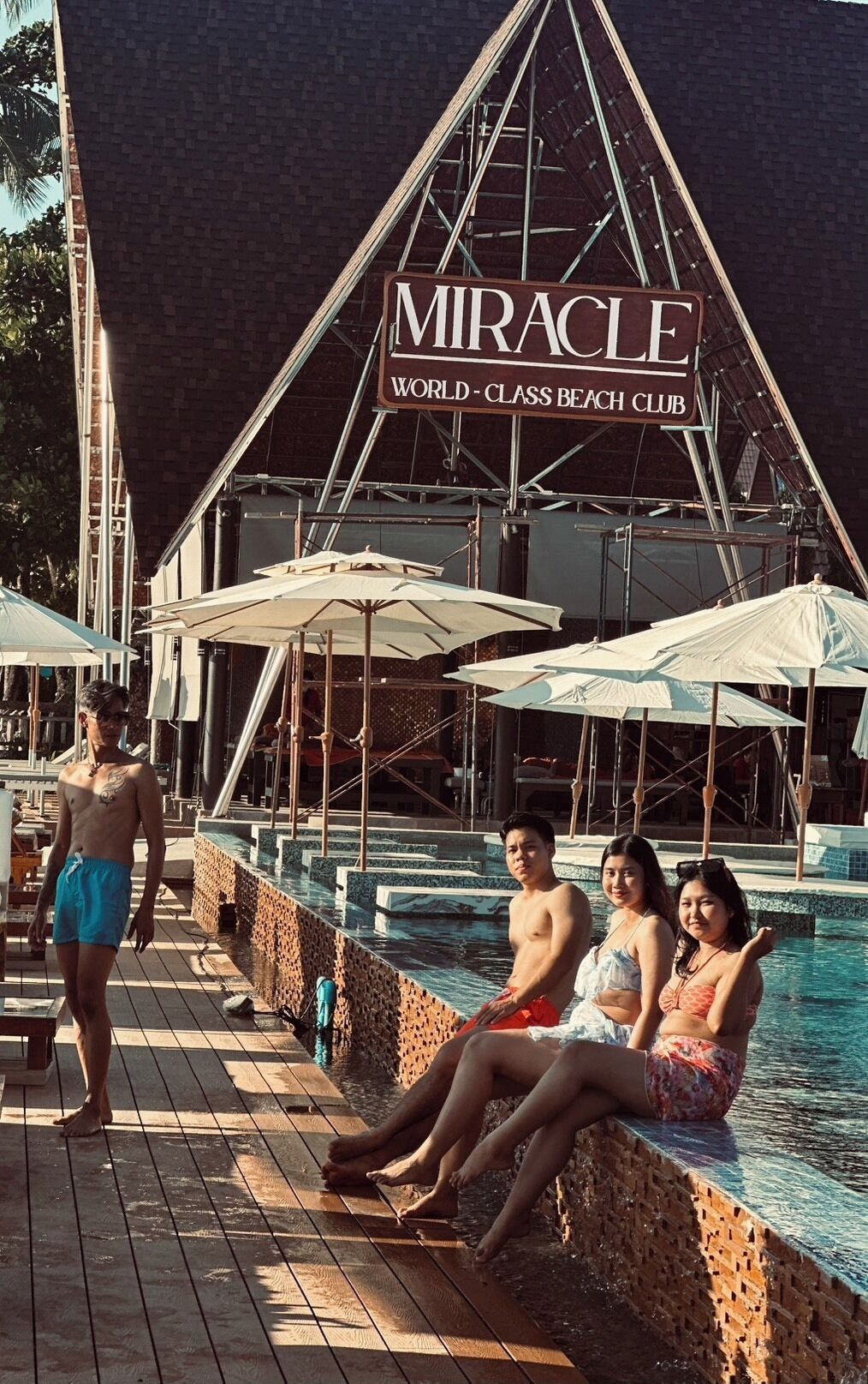 A poolside area with a sign reading "Miracle World-Class Beach Club".