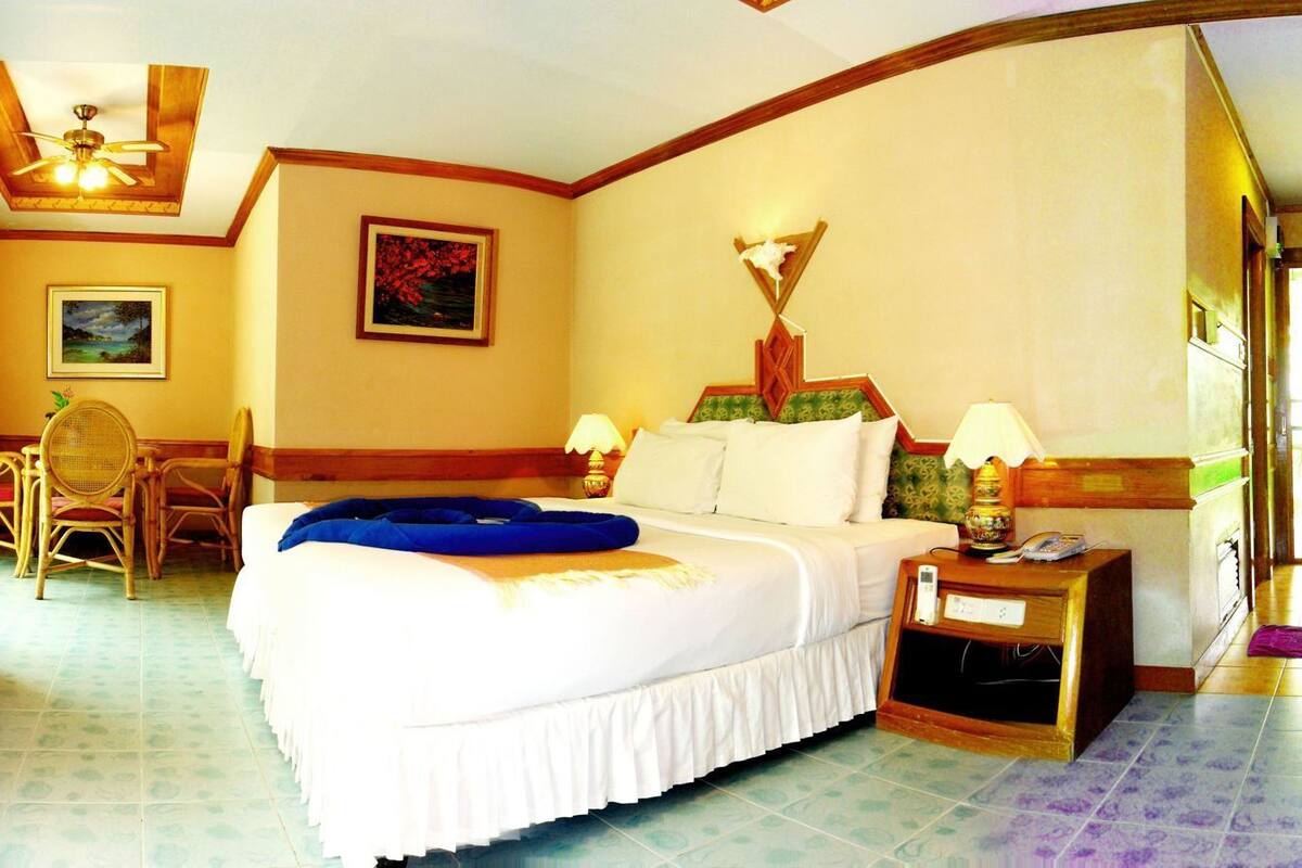 A hotel room with a bed, a desk, a chair, a lamp, a nightstand, a television, and a refrigerator.