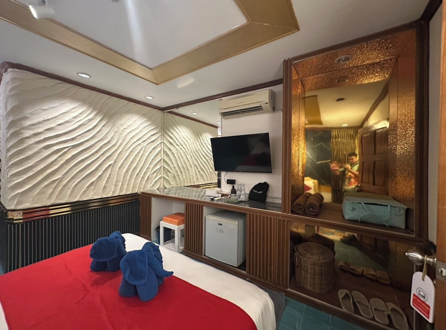 Habitación de hotel con cama, televisión, escritorio pequeño, espejo y vista al baño.