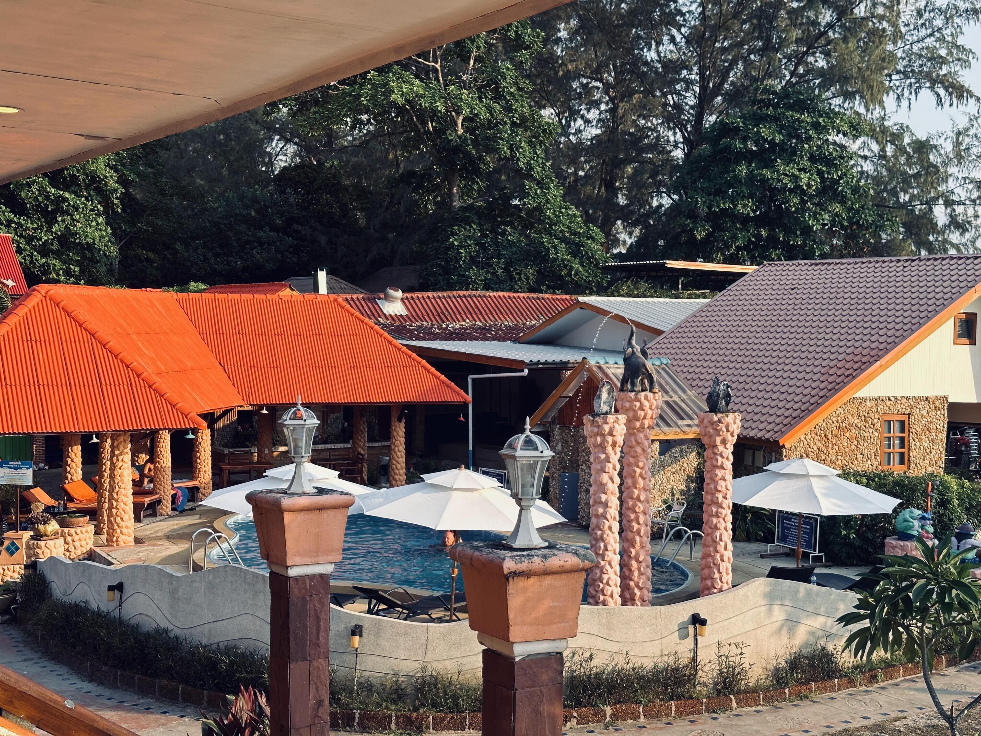Zona de piscina con sombrillas, sillas de descanso y una fuente de piedra.